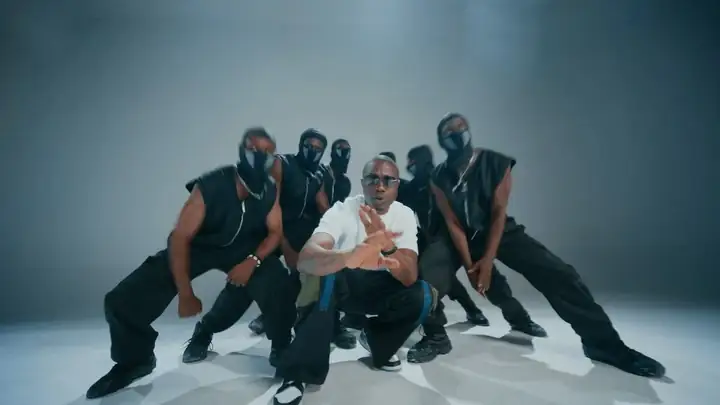 Corto Alto and his dancers in black, crouched in formation on a white studio floor, from the “GO” video